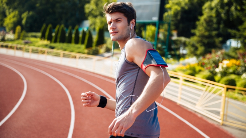 Man runs on a track with earphones and an armband for his race day playlist