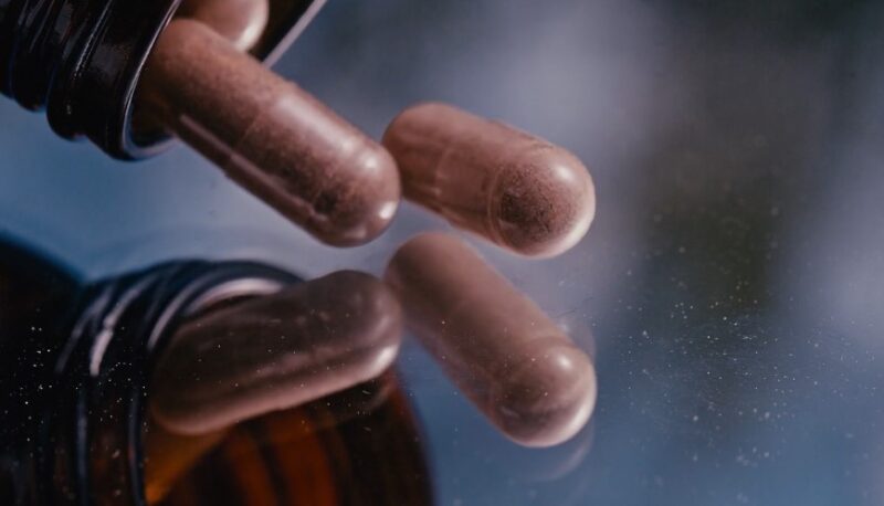 Brown capsules gently detach from a dark bottle