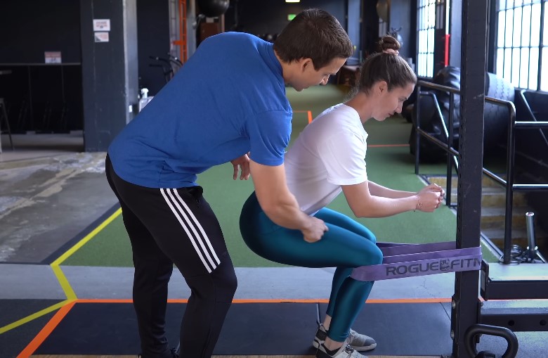 A personal trainer guides a client through a controlled squat