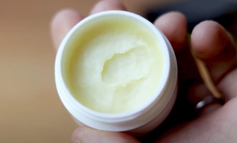 Creamy, light-yellow balm in a small, white container