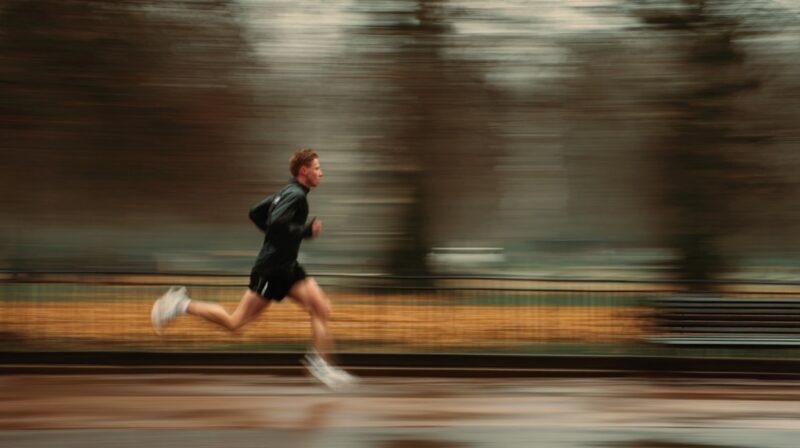 Runner in motion blur sprinting in a park wearing a black jacket and shorts