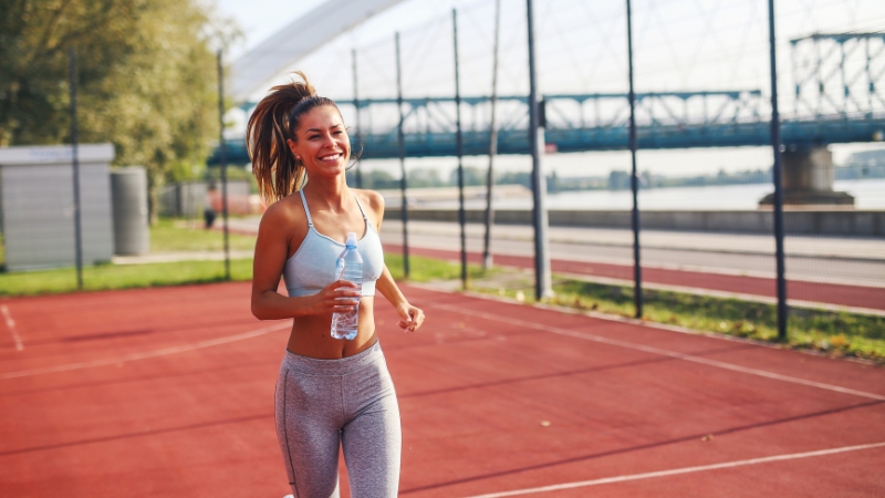Smiling woman jogging on a track with water in hand during week 7 of half marathon training