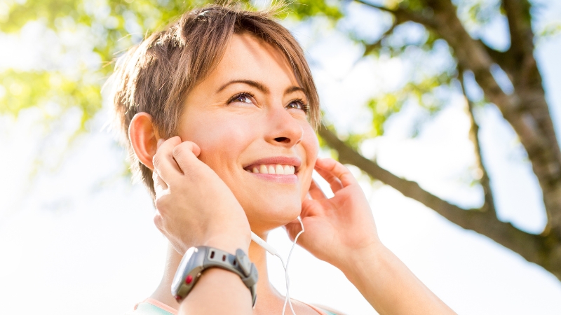 Woman smiles as she puts on earphones to enjoy music before a run