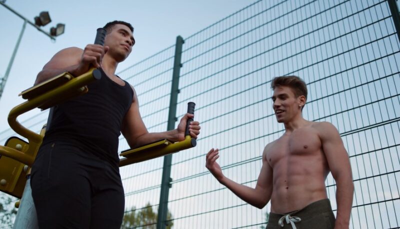Two men engage in a workout outdoors, utilizing a pull-up bar