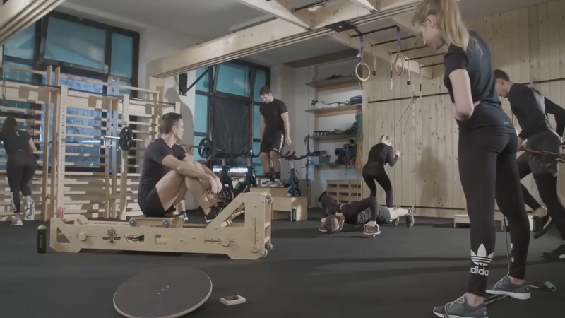A group of people train in a gym with various equipment under the guidance of a coach