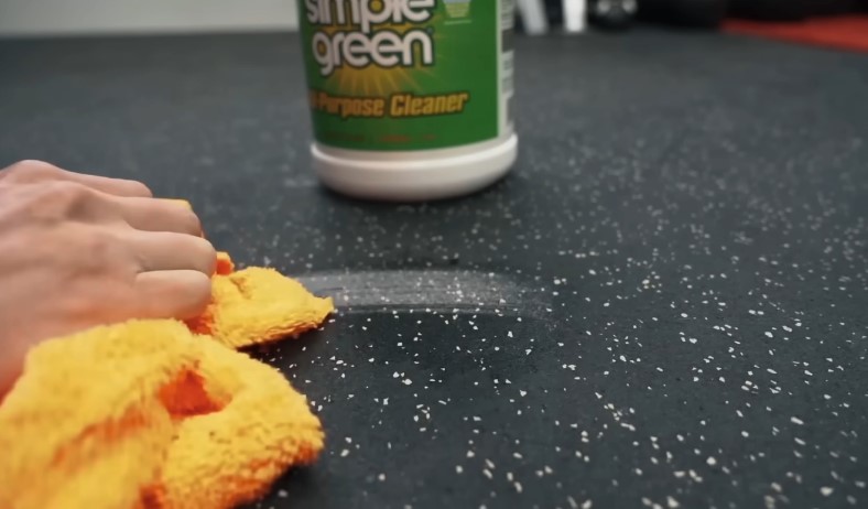 A hand meticulously cleans a gym floor with a yellow cloth and Simple Green cleaner