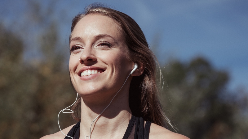 Woman smiling with earphones during an outdoor run, showing the energy of a morning runner