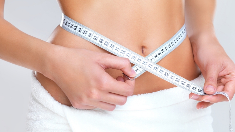 A woman measures her waist with a tape measure, illustrating the concept of ideal weight for women in their 30s
