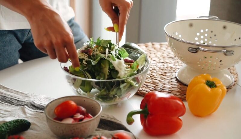 A colorful array of vegetables—peppers, tomatoes, and radishes—surround a bowl of mixed greens