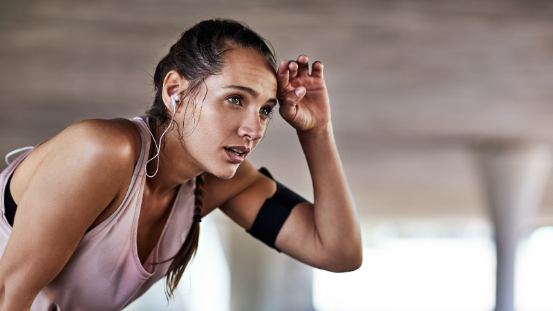 Woman catching her breath after a workout, listening to music with earbuds, mid-reset routine