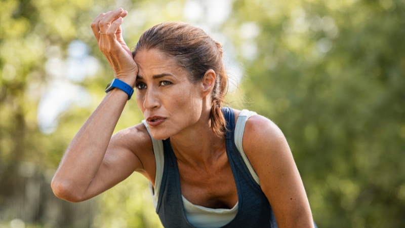 Woman wiping sweat from her forehead after exercising outdoors, catching her breath during post-workout recovery