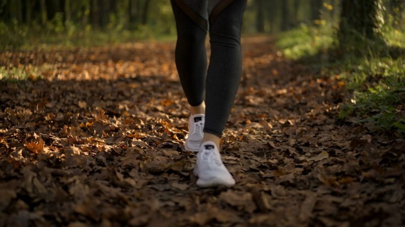 Close-up of a person’s legs walking briskly on a forest trail covered with leaves