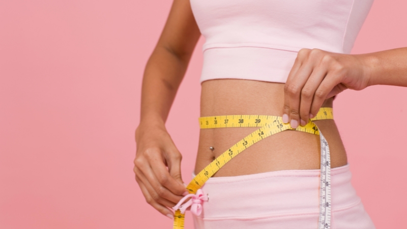A woman in pink activewear checks her waist with a measuring tape