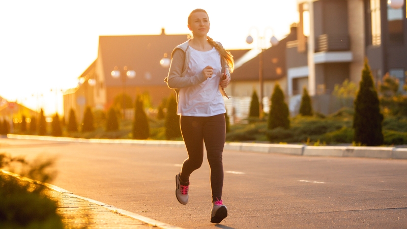 Woman jogging on a quiet street at sunrise, showing the effort of morning running