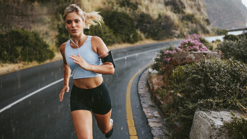 A woman runs along a scenic road in the rain