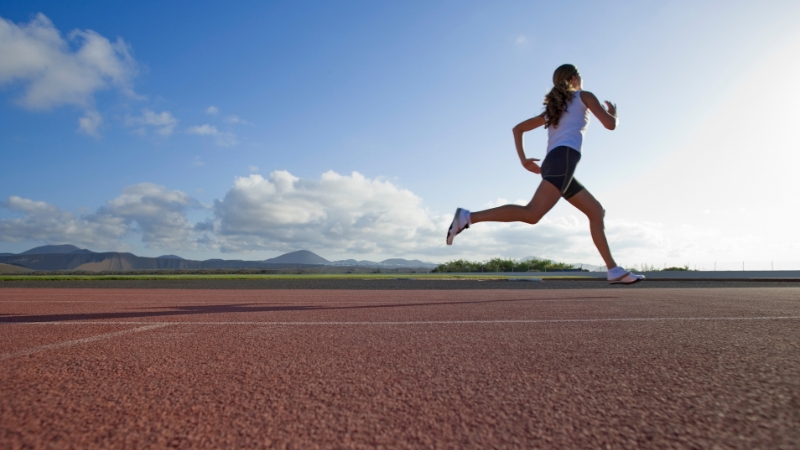Woman running on a track under blue sky for inspiring running quotes