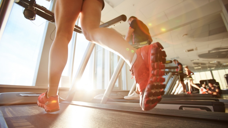 Person running on a treadmill in a bright gym with sunlight coming through the windows