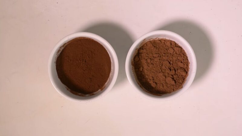 Two small bowls filled with cocoa powder, one darker and finer, the other lighter and coarser in texture