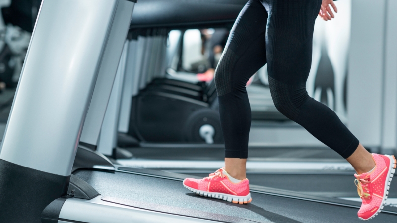 Person running on a treadmill in bright pink shoes inside a gym