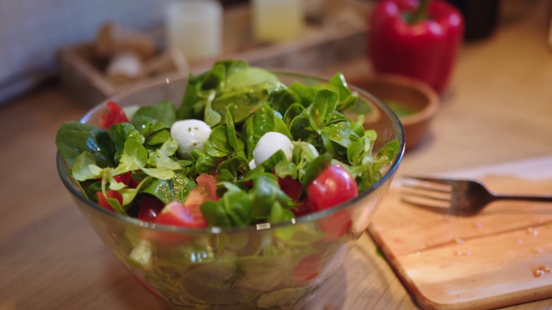 A fresh salad with leafy greens, cherry tomatoes, and mozzarella balls served in a glass bowl