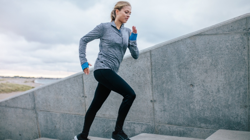 Woman running up outdoor concrete steps, illustrating effort and calorie calculation in action
