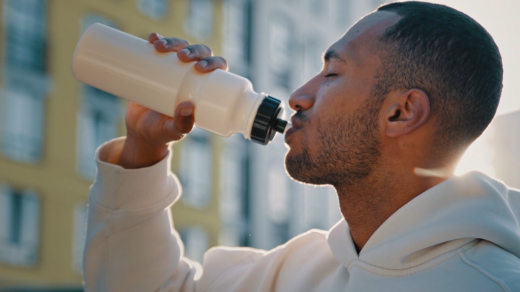 Athlete drinking from a sports bottle outdoors after training, staying hydrated