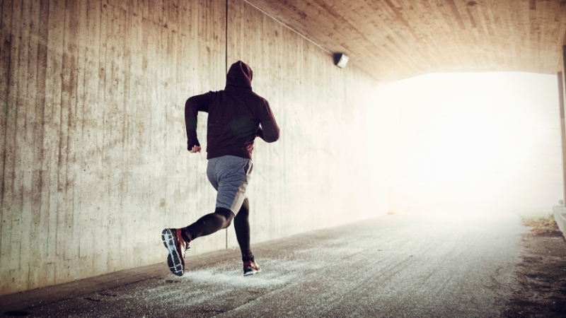 A runner in a hoodie moves through a tunnel toward the light