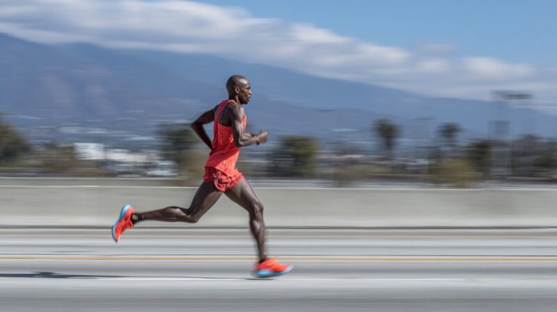 Runner in a red outfit sprinting on a city road with mountains and palm trees blurred in the background, symbolizing speed and focus