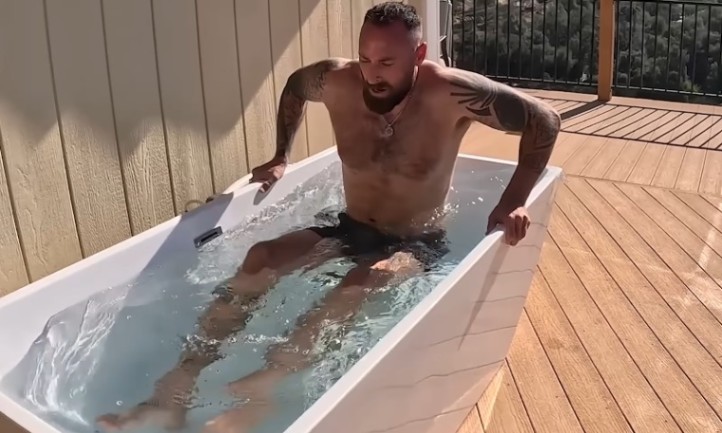 A man sits in a bathtub on a wooden deck