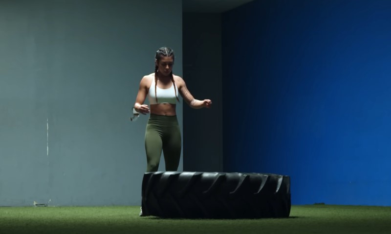 A woman stands on a large tire in an indoor gym