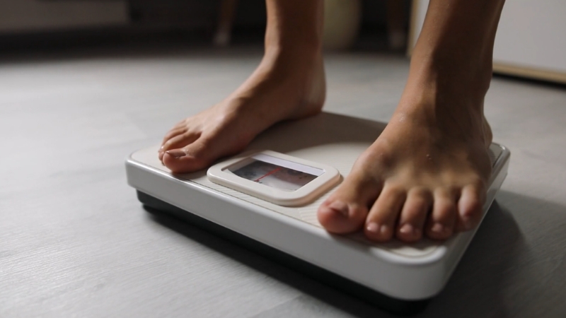 A person standing on a bathroom scale to track weight loss linked to lower CRP levels