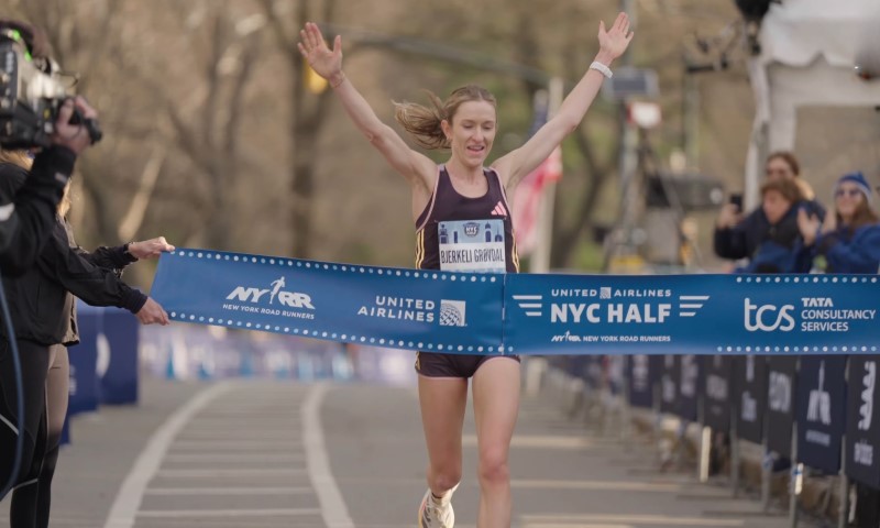 Runner crossing the finish line with arms raised in victory at the NYC Half Marathon