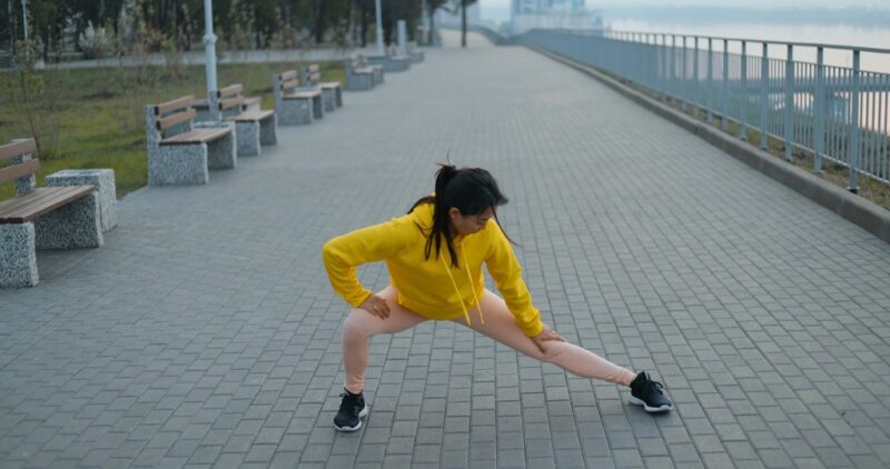Outdoor stretching exercise performed on a paved walkway near a railing
