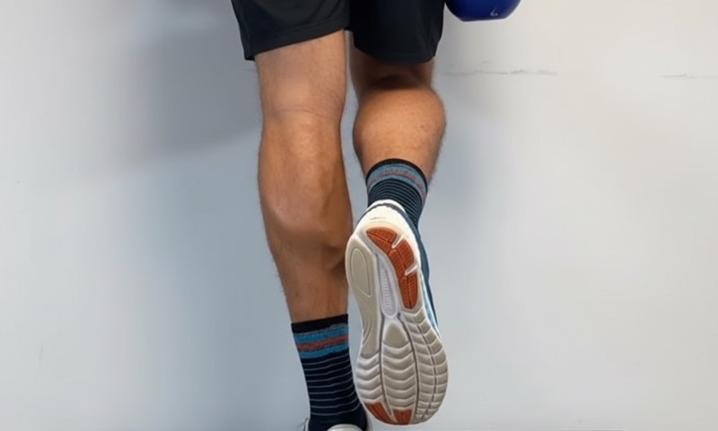 A person in shorts and striped socks lifts one leg, showing the sole of a sneaker against a plain white background