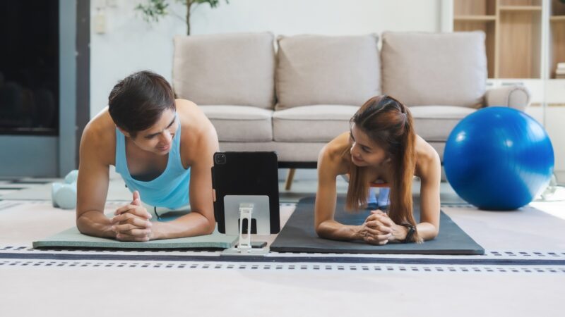 Two people hold planks on exercise mats during a home workout